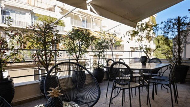 An outdoor patio with round tables and chairs, potted plants, and a view of a residential area. - Art Deco Apt in Kolonaki (Athina)