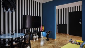 A modern living room with a striped wall, a round glass table, and a flat-screen TV. - Art Deco Apt in Kolonaki (Athina)