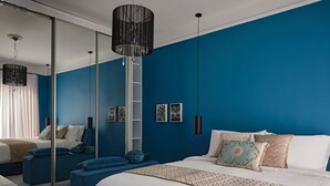 A modern bedroom with a large bed, a mirror, a blue accent wall, and a black chandelier. - Art Deco Apt in Kolonaki (Athina)