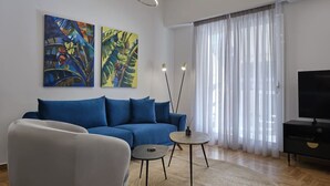 Ein modernes Wohnzimmer mit einer Couch, zwei Beistelltischen, einem Fernseher und abstrakten Bildern an der Wand.