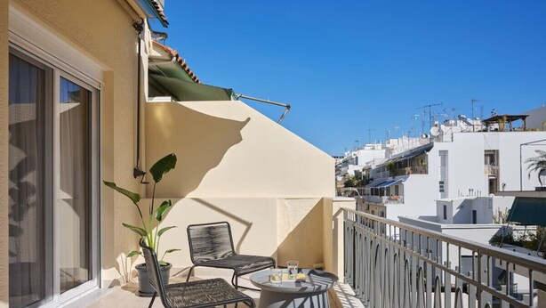 Ein Balkon mit zwei Stühlen, einem Tisch, einem Blumentopf und Blick auf angrenzende Gebäude.