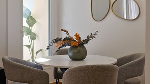 Ein Essbereich mit einem runden Tisch, zwei Stühlen, einer Blumenvase und zwei Wandspiegeln.