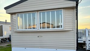 A single-story mobile home with a flat roof, a large window, and a small porch area. - 3 bed Stunning Caravan Situated nr Whitstable (Whitstable)