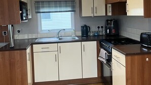 A compact kitchen with white and wooden cabinets, a built-in oven, a sink, and a window with blinds. - 3 bed Stunning Caravan Situated nr Whitstable (Whitstable)