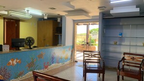A reception area with a tiled mosaic wall, wooden furniture, and a fan. - Clube Praiano (Cabo Frio)