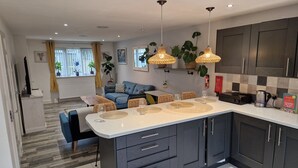 A modern kitchen with dark cabinets, a large island, and pendant lighting. - Charming 3-bed House in Newquay (Newquay)