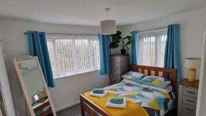 A bedroom with a bed, a dresser, a mirror, and a window with curtains. - Charming 3-bed House in Newquay (Newquay)