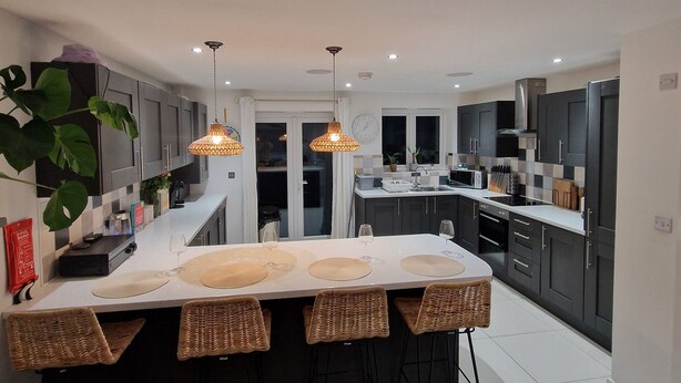 A modern kitchen with a central island, pendant lighting, and dark cabinetry. - Charming 3-bed House in Newquay (Newquay)