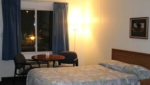 Ein Hotelzimmer mit einem Bett, einem Tisch mit zwei Stühlen, einem Vorhangfenster und einer Wandlampe.