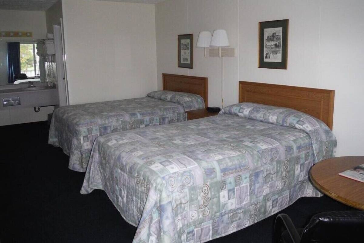 Une chambre d’hôtel avec deux lits, une table ronde, une chaise, un miroir et une fenêtre.