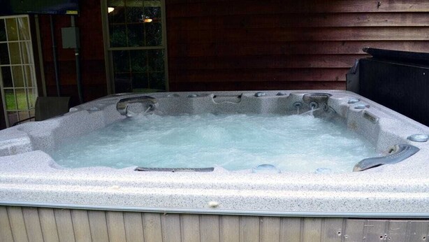 A hot tub with a stone exterior, positioned outdoors against a wooden wall.