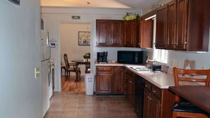 A kitchen with wooden cabinets, a microwave, and a coffee maker. There is a dining area with a table and chairs.