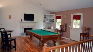 A living room with a pool table, a fireplace, a television, and a bookshelf.