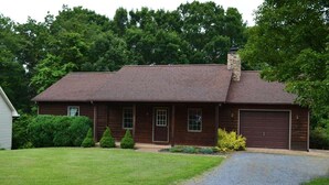 A two-story log cabin with a stone chimney, a front garage, and a well-maintained lawn.