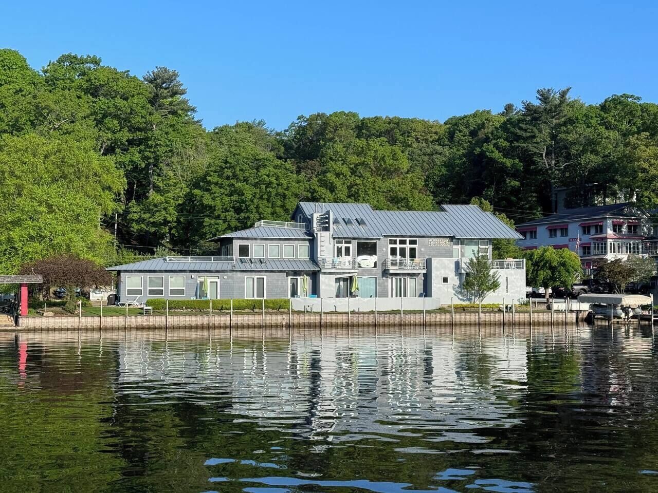 A waterfront property with a large house featuring multiple levels, a dock, and a reflection in the water.
