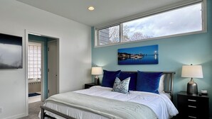 A bedroom with a bed, two bedside tables, a nightstand, a window, and a painting on the wall. - Stunning 3BR Condo w/6 Decks & a Boat Dock (Saugatuck)