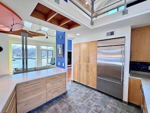 A modern kitchen with a stainless steel refrigerator, wooden cabinets, and a large island with drawers.