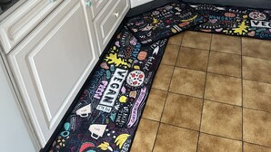 A kitchen with white cabinets, a black countertop, and a colorful rug.