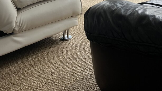 A living room with a white sofa, a glass coffee table, a black ottoman, a television, and a radiator.