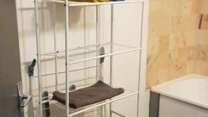 A metal bunk bed with towels, a small shelf, and a trash bin in a room with wooden flooring and a white wall.