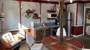 Une cuisine compacte comprenant une table à manger en bois, un four à micro-ondes, un réfrigérateur et un petit coin salon avec une chaise et un canapé.