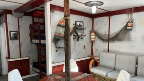 Une pièce avec une table ronde en bois, des chaises blanches, un canapé, une échelle, un hamac et un gilet de sauvetage.
