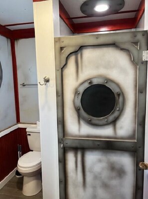 Un baño con una puerta decorada con motivos náuticos, un inodoro y una zona de ducha.