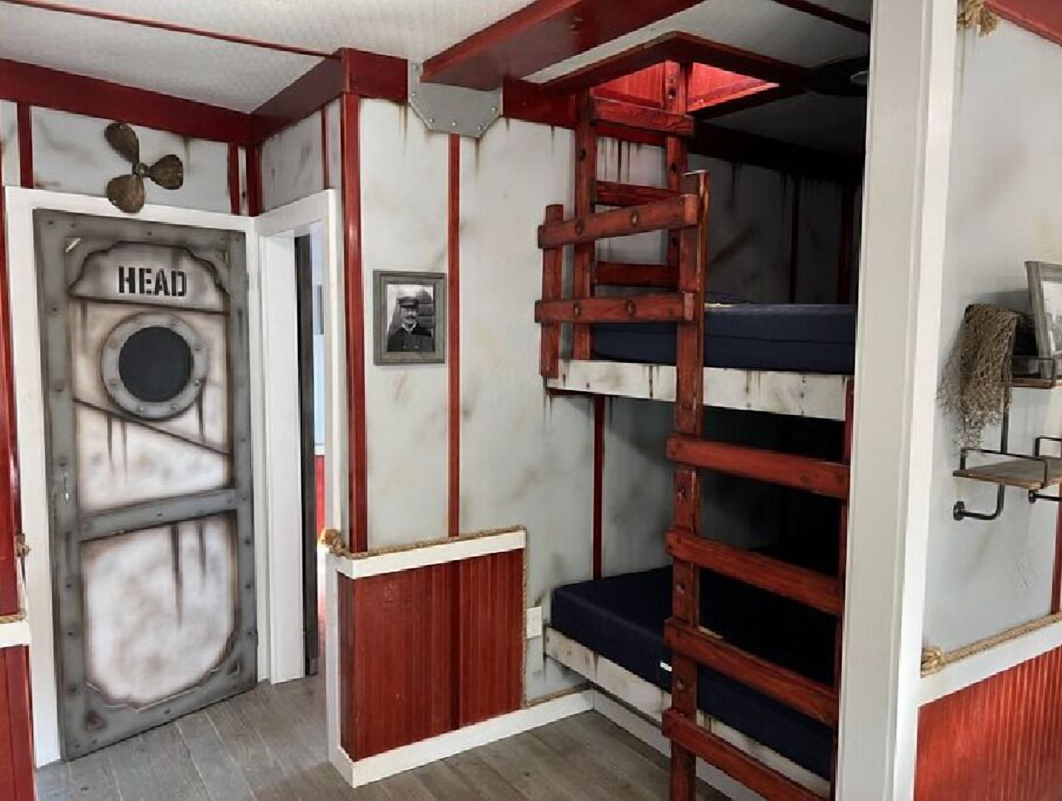 A bunk bed room with a ladder, a door labeled "HEAD", and a small shelf with a plant.