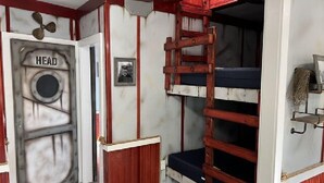 Une chambre avec un lit superposé, une échelle, une porte sur laquelle est écrit « TÊTE » et une petite étagère avec une plante.