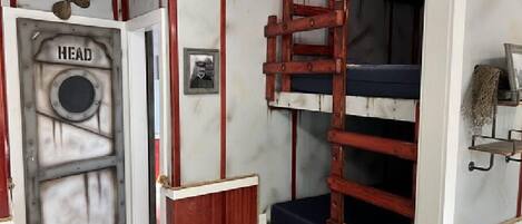 A bunk bed room with a ladder, a door labeled "HEAD", and a small shelf with a plant.