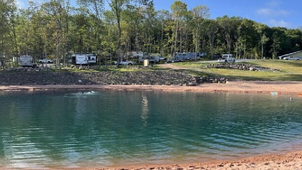 Un terrain de camping avec des emplacements pour camping-cars et des zones pour tentes, une plage de sable et un lac paisible.