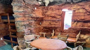 Un interior rústico de piedra con una mesa redonda de madera y sillas, una escalera y una ventana con cortinas.