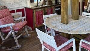 Une cuisine rustique avec une table et des chaises en bois, une étiquette avec un numéro suspendue, et une fenêtre avec des rideaux.