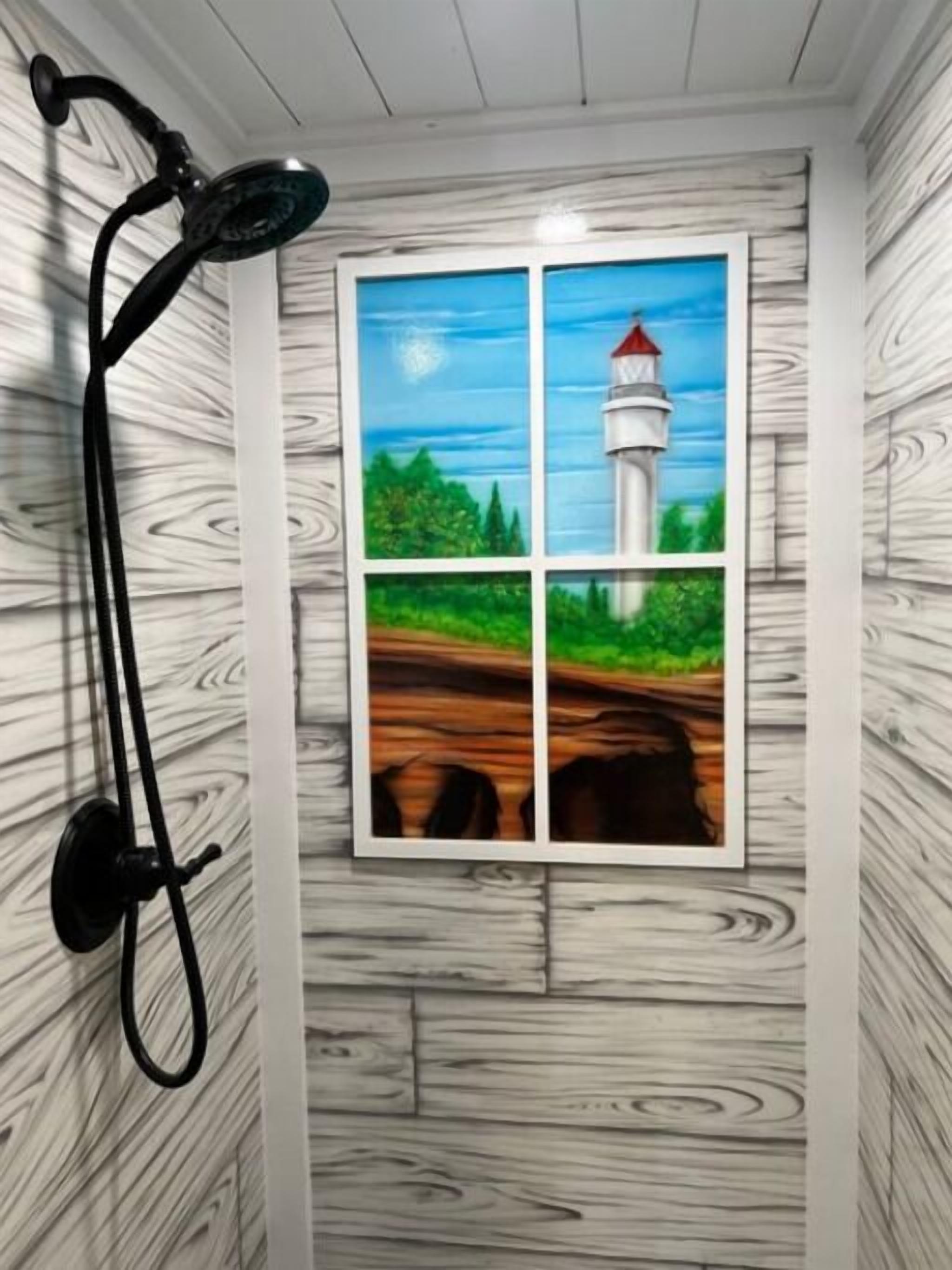 Un baño con un diseño de pared de madera, un cabezal de ducha y un ventanal con una pintura de un faro.