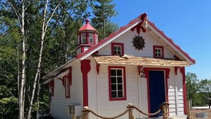 Un petit bâtiment d’un seul étage, avec un toit rouge et des murs blancs, une porte bleue et des fenêtres dotées de bordures rouges.