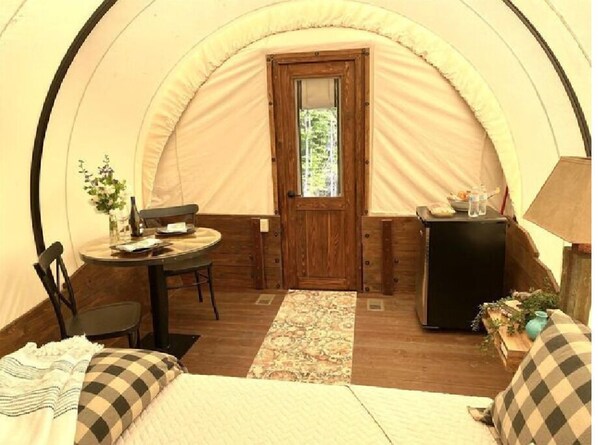 A tent with a wooden door, a table with chairs, a small cabinet, and a bed with checkered pillows.