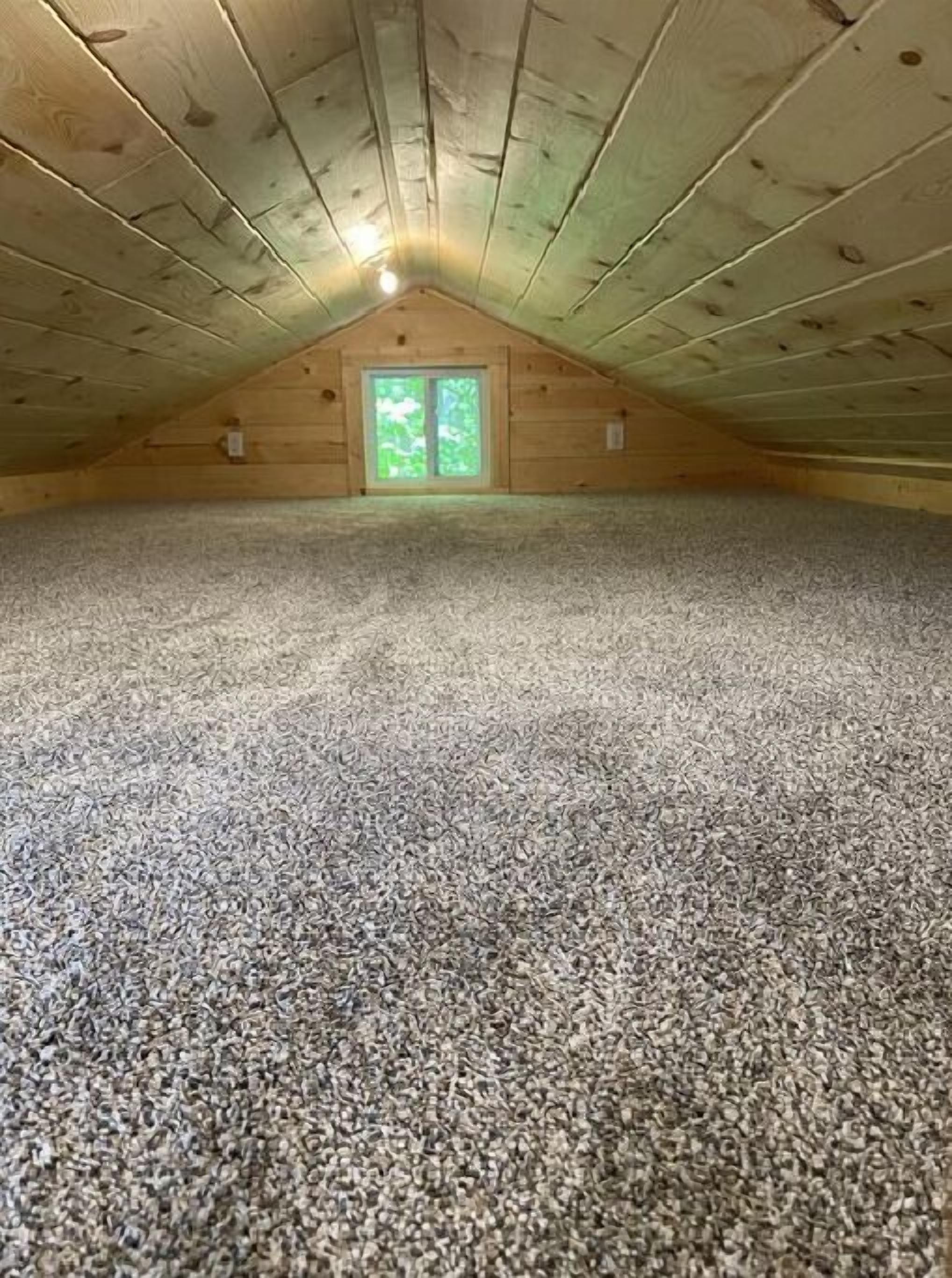A spacious attic room with a sloped ceiling, a large window, and a carpeted floor.