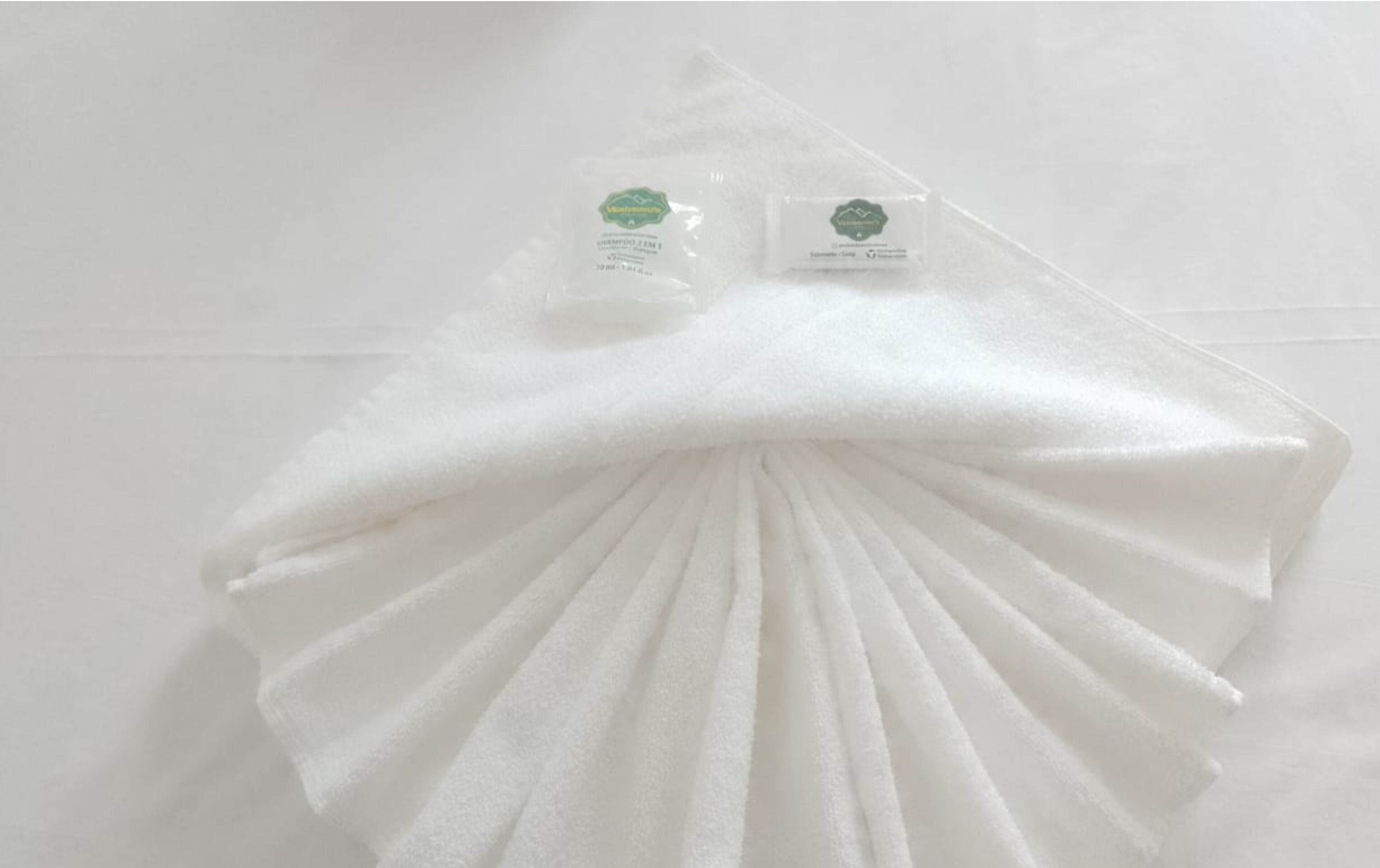 A white towel folded in a fan shape with two small plastic bags containing white towels on top.