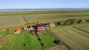Eine Vogelperspektive auf eine ländliche Landschaft mit einem großen Haus, umgeben von Feldern und einem Gewässer in der Ferne.