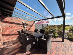 An outdoor patio with a glass enclosure, wicker furniture, and a brick wall.