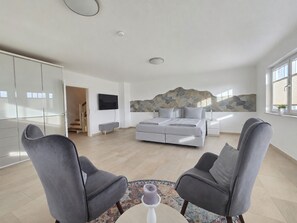 A modern bedroom with a stone accent wall, a bed, a TV, and a view of a staircase.