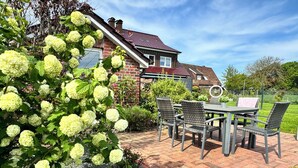 Eine Terrasse mit Steintisch und -stühlen, umgeben von Grünpflanzen und einem Haus im Hintergrund.