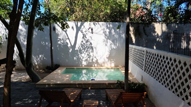 Un área de piscina pequeña al aire libre con terraza de madera y dos sillas reclinables.