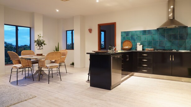 A modern kitchen with a black island, teal backsplash, and a large window overlooking a cityscape. - Tuscan Villa with a view. (Havelock North)