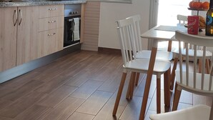 A modern kitchen with wooden cabinets, a built-in oven, and a dining area with white chairs and a table. - Carmen´s House (Arico Viejo)