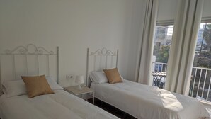 Two single beds with white linens and brown pillows, a bedside table with a lamp, and a balcony with a railing. - Carmen´s House (Arico Viejo)