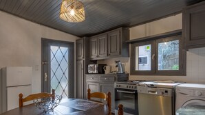 Une cuisine moderne avec des meubles gris, une table à manger avec des chaises, un luminaire suspendu et des appareils électroménagers intégrés, notamment une cuisinière, un four et un lave-vaisselle.