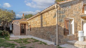 Un bâtiment en pierre avec un toit en tuiles, une porte en bois et un petit jardin agrémenté de gravier et de gazon.