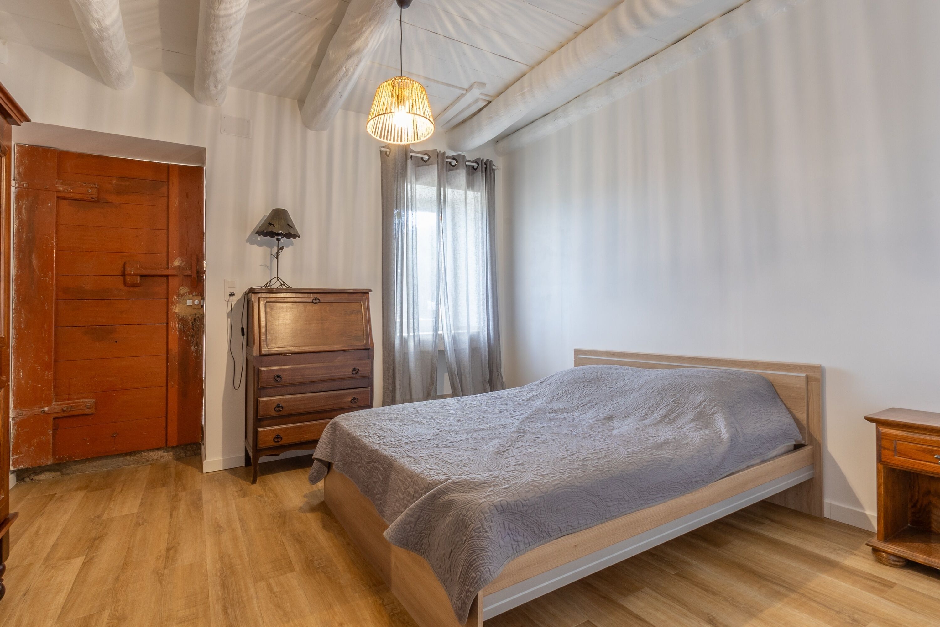 A bedroom with a wooden bed, a wooden dresser, a lamp, and a door.