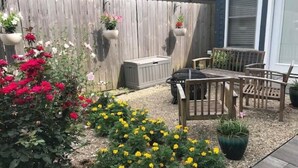 En terrasse med et træbord og stole, omgivet af en have med gule og røde blomster.